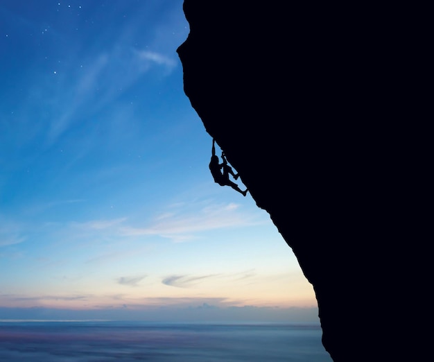 Vista de ângulo baixo de um homem em silhueta escalando montanhas contra o céu azul