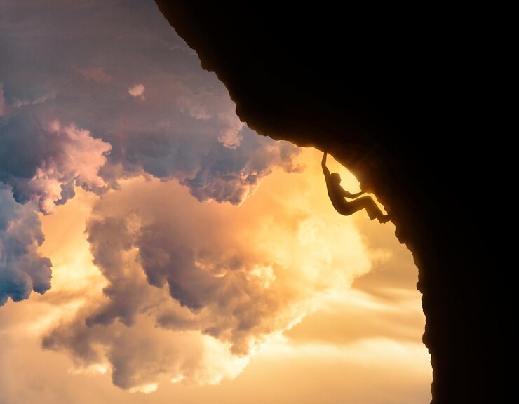 Foto vista de ângulo baixo de um homem em silhueta escalando uma montanha contra o céu durante o pôr do sol