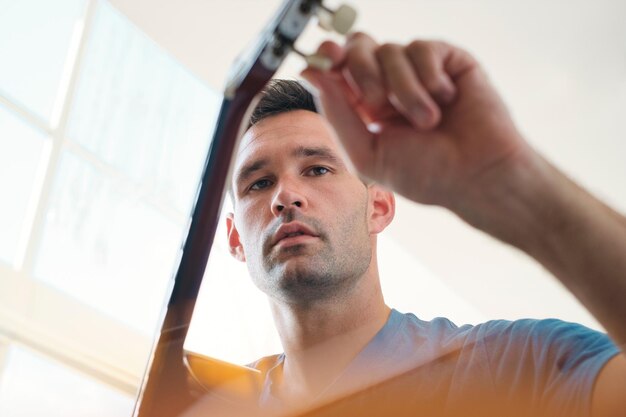 Foto vista de ângulo baixo de um homem segurando uma guitarra sentado em casa