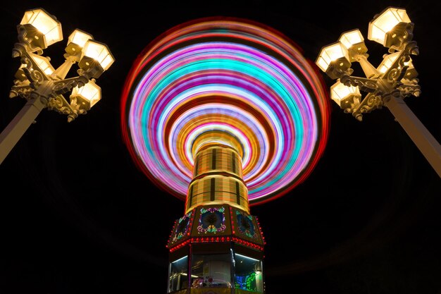 Foto vista de ângulo baixo de um parque de diversões iluminado em meio a um poste de lâmpada