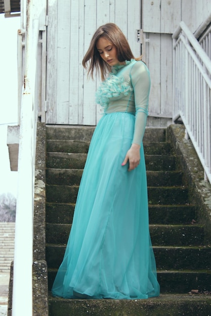 Foto vista de ângulo baixo de uma bela mulher vestindo um vestido azul enquanto está de pé nas escadas