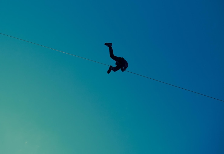 Foto vista de ângulo baixo de uma pessoa fazendo uma corda apertada caminhando contra um céu azul claro