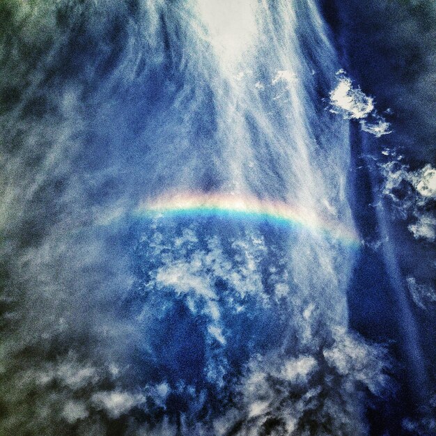 Foto vista de ângulo baixo do arco-íris contra o céu nublado azul