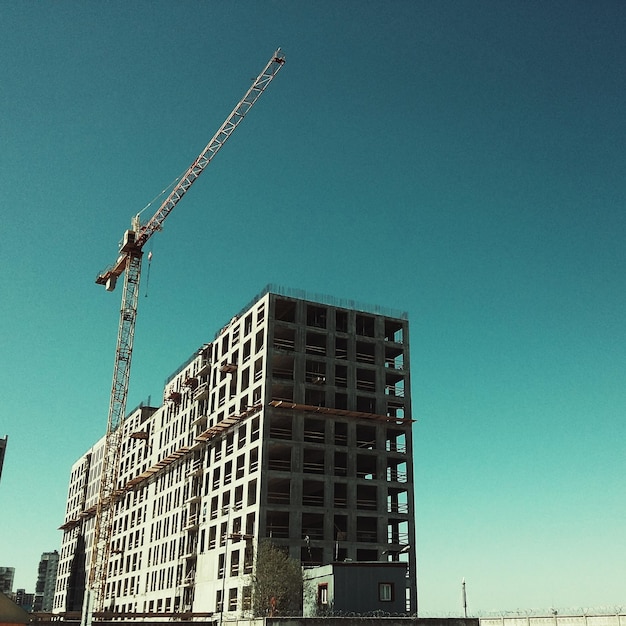 Vista de ângulo baixo do guindaste por edifícios incompletos contra um céu claro