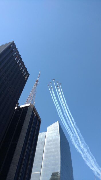 Foto vista de ângulo baixo do show aéreo por edifícios contra o céu claro na cidade