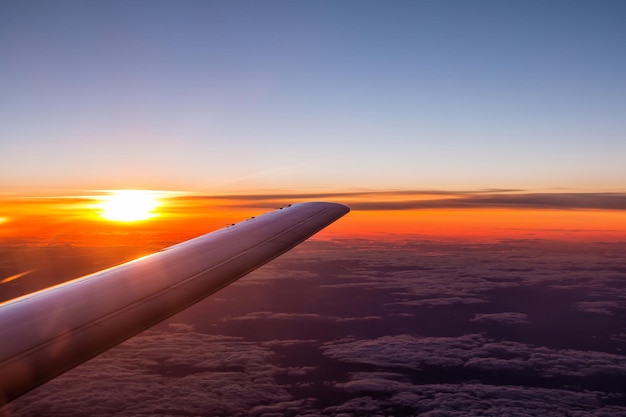 Vista de asa de avião voando acima das nuvens no céu ao pôr do sol