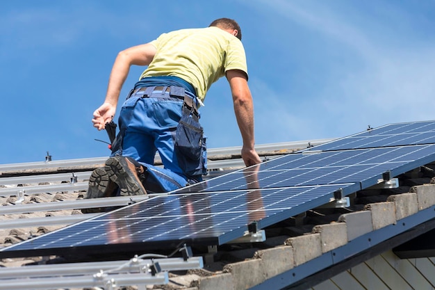 Vista de baixo ângulo de homem instalando painéis solares no telhado contra o céu