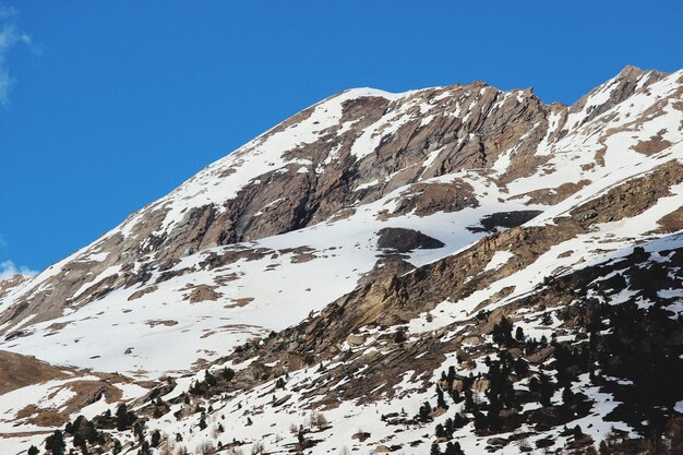 Vista de baixo ângulo de montanhas cobertas de neve contra um céu azul claro