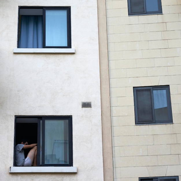 Vista de baixo ângulo do homem sentado no peitoril da janela do edifício