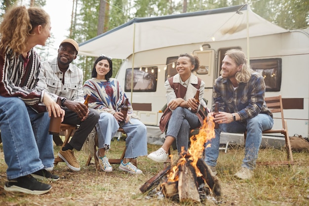 Vista de baixo ângulo em diverso grupo de jovens modernos, desfrutando de acampar ao ar livre com a van de reboque e ...