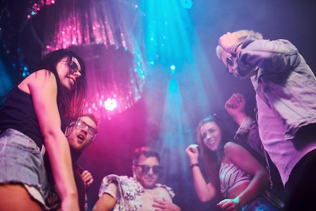 Vista de baixo de jovens que se divertem na boate com luzes laser coloridas