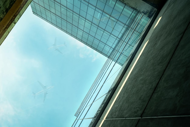 Vista de baixo para cima do moderno prédio de escritórios de vidro sustentável e avião voando no exterior do céu azul
