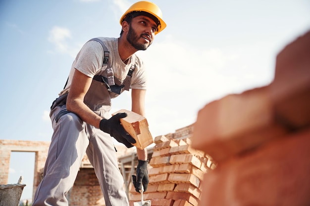 Foto vista de baixo tijolo na mão homem indiano bonito está no canteiro de obras