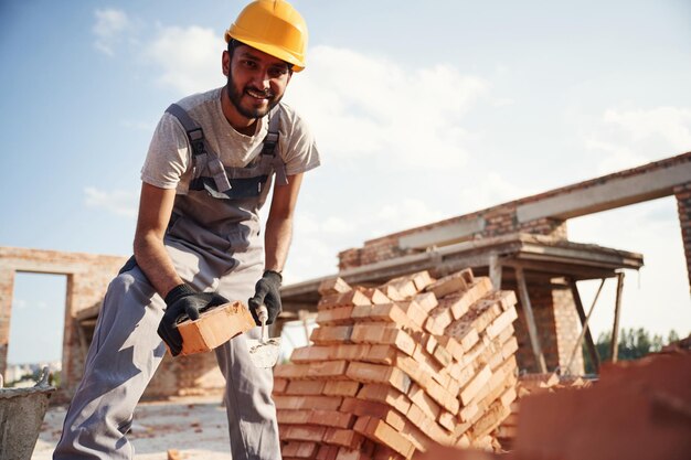 Foto vista de baixo tijolo na mão homem indiano bonito está no canteiro de obras