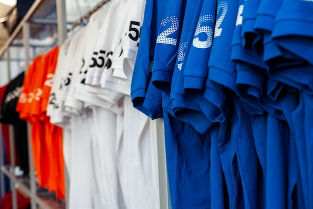 Foto vista de camisetas coloridas em cabides expostos em uma loja de roupas