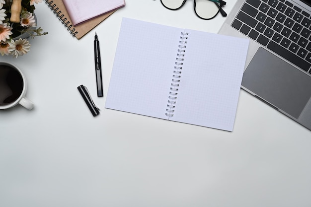 Vista de cima caderno em branco laptop copos e xícara de café em escritório branco Copiar espaço para o seu texto