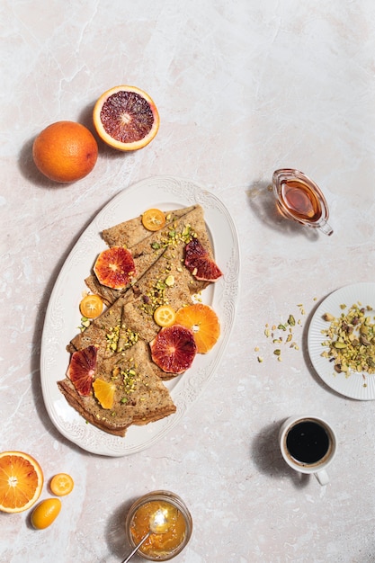 Vista de cima crepes com laranja de sangue, mel e geléia na mesa de mármore, café da manhã doce, sombras duras