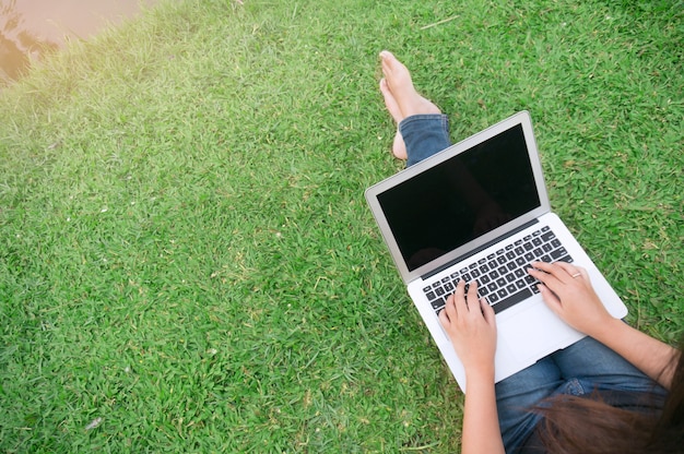 Vista de cima da mulher sentada no parque na grama verde com laptop, estudante estudando ao ar livre. Copie espaço para texto.