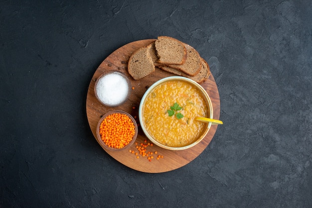 Vista de cima da sopa de lentilhas com lentilhas crus salgadas e pães escuros na superfície escura