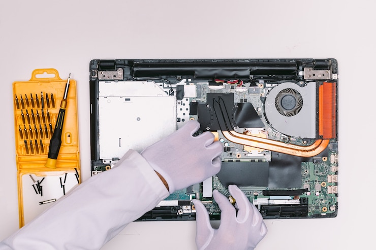 Foto vista de cima das mãos enluvadas de um engenheiro, colocando um disco rígido ssd em um laptop em uma mesa branca