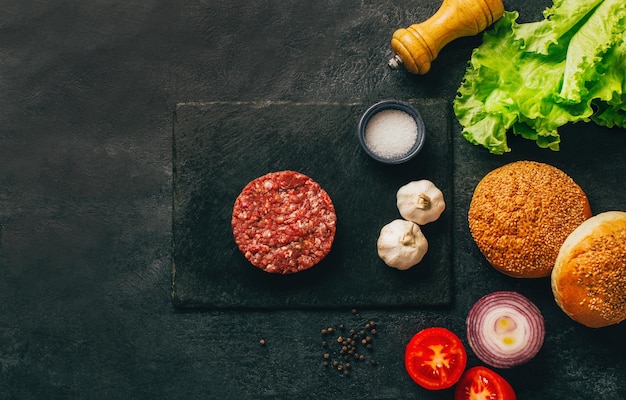 Foto vista de cima de ingredientes de hambúrguer carne crua pães legumes condimentos em mesa escura com espaço livre para texto