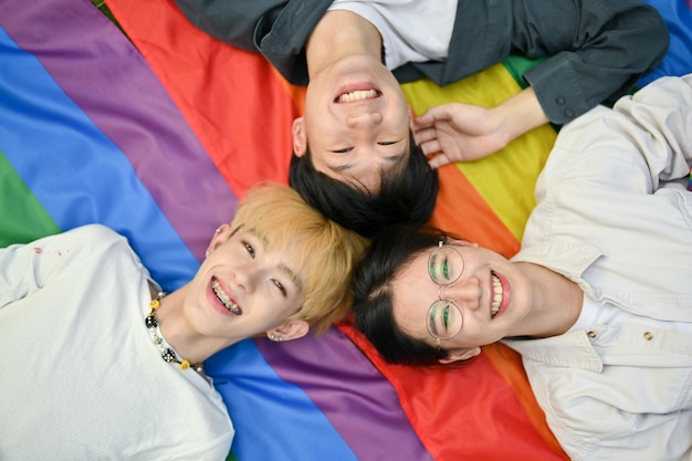 Vista de cima de jovens e alegres amigos asiáticos deitados juntos em uma bandeira do arco-íris LGBT