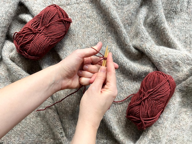 Foto vista de cima de mãos de mulheres moldadas em loops de fios de lã vermelha para tricô com fios vermelhos