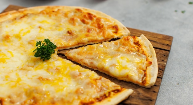 Vista de cima de um delicioso e suculento pedaço fatiado de queijo duplo, massa italiana tradicional, pizza fina e crocante fora do forno, colocada em uma tábua de corte de madeira, pronta para servir na mesa para o jantar