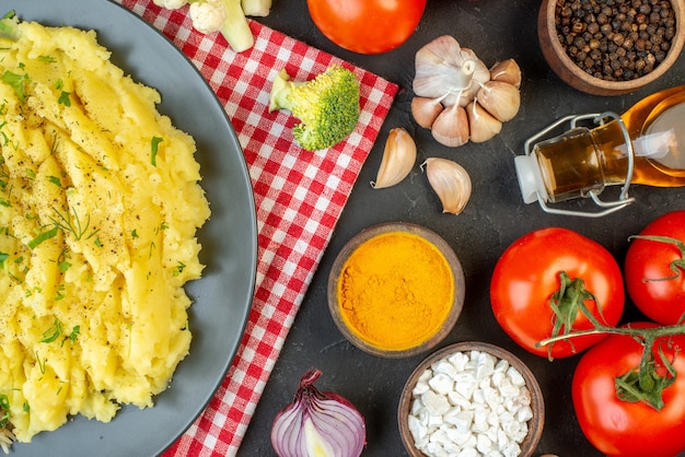 Vista de cima de um delicioso jantar com purê de batata em um prato sobre uma toalha vermelha despojada e especiarias de legumes frescos garrafa de óleo de limão caído em fundo preto