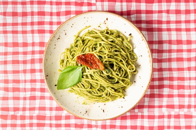 Vista de cima de um delicioso prato de pasta de pesto decorado com uma folha de manjericão e um tomate secado ao sol