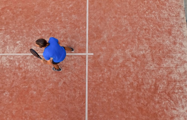 Vista de cima de um jogador de paddle esperando a bola em uma partida em uma quadra ao ar livre.