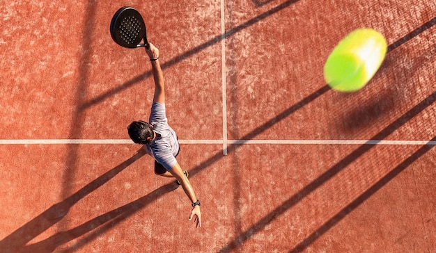 Vista de cima de um jogador de paddle profissional que acaba de acertar a bola durante uma partida ao ar livre. A bola passa perto da câmera.