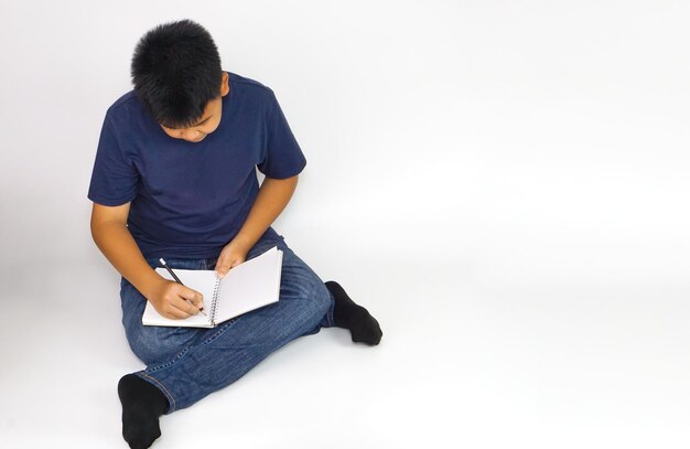 Vista de cima de um menino sentado alegremente escrevendo um livro Educação e conceito de aprendizagem