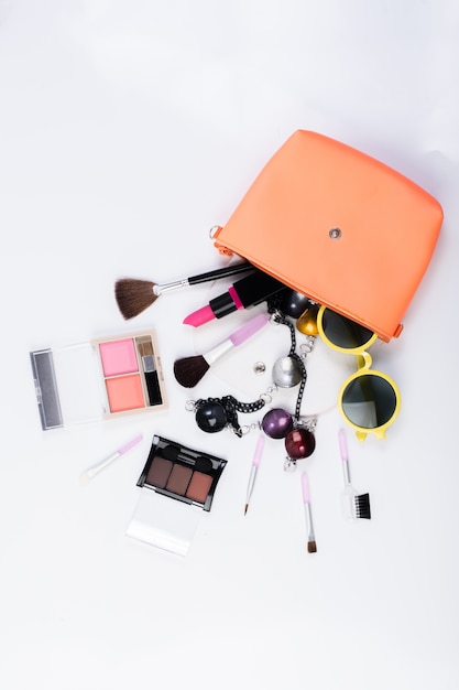 Vista de cima de um saco de maquiagem, com produtos cosméticos de beleza espalhando-se sobre um fundo branco.