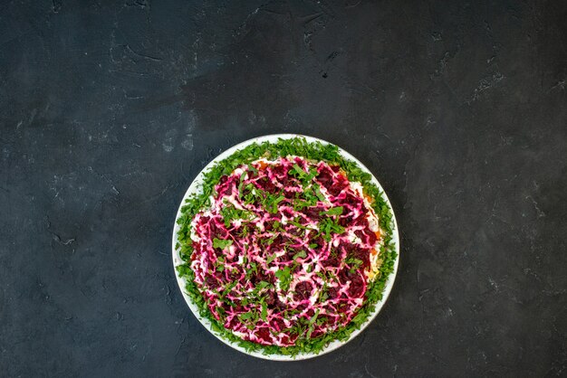 Vista de cima de uma deliciosa salada decorada com verde em um prato branco sobre fundo preto com espaço livre