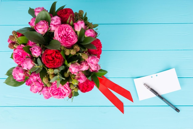 Vista de cima de uma etiqueta de presente em branco com uma caneta perto de buquê de rosas cor de rosa e vermelhas. Dia dos namorados e conceito de aniversário