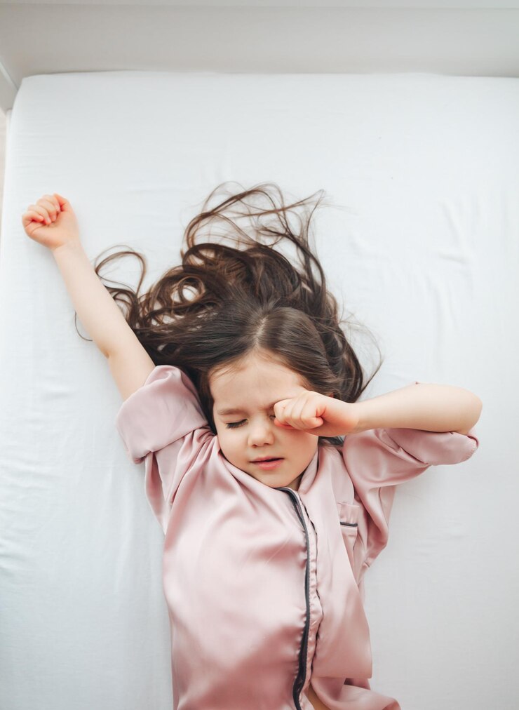 Foto vista de cima de uma menina bonitinha se esticando em uma cama branca acordando de manhã o conceito de ir para a cama acordando e relaxando