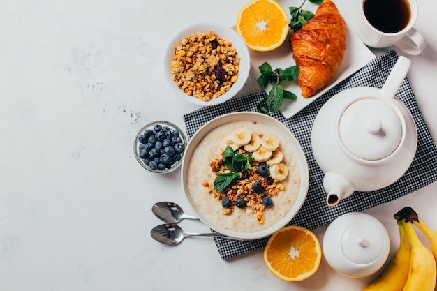 Foto vista de cima de uma mesa branca com farinha de comida com frutas e nozes frutas bagas chá hortelã laranjas bananas pratos de chá com espaço livre