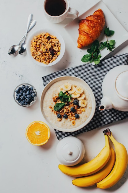 Vista de cima de uma mesa branca com farinha de comida com frutas e nozes frutas bagas chá hortelã laranjas bananas pratos de chá com espaço livre