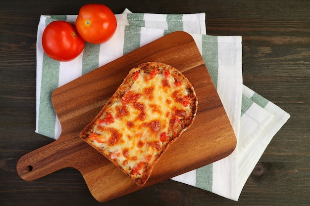 Vista de cima de uma torrada de pizza caseira recém-assada na tábua de pão com tomates frescos