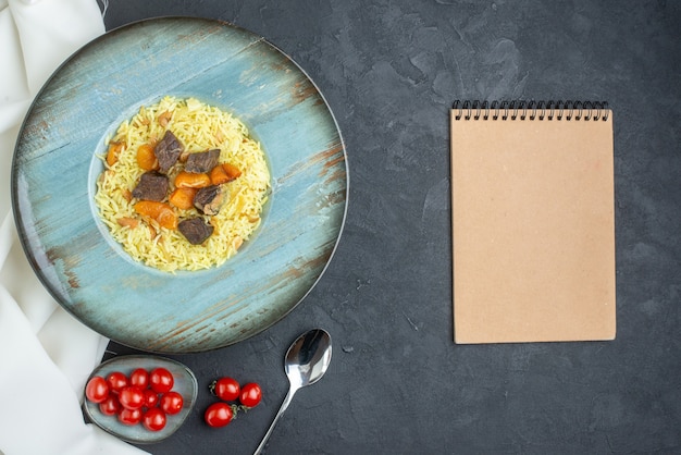 Vista de cima, delicioso pilaf cozido de arroz com damascos secos e fatias de carne dentro do prato em superfície escura