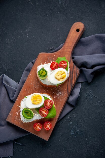 Vista de cima deliciosos sanduíches com tomates pepinos e ovos na tábua fundo escuro refeição hambúrguer comida almoço sanduíche torrada lanche