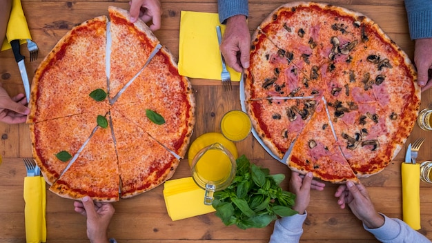 Vista de cima e de cima de duas grandes pizzas ou pizzas familiares cozinhadas para comer juntos em casa na mesa de madeira - família comendo e bebendo juntos