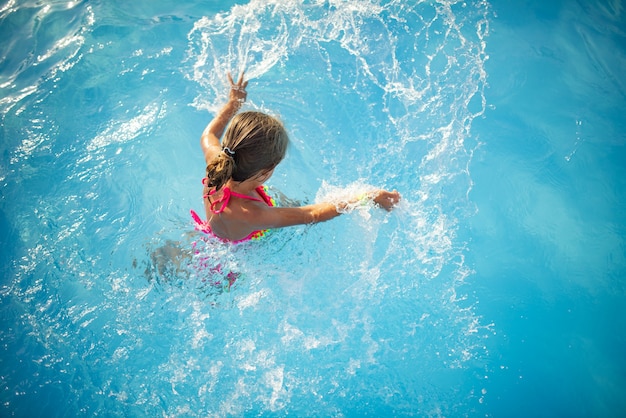 Vista de cima, garotinha feliz em trajes de banho de cor brilhante nadando na piscina clara e quente