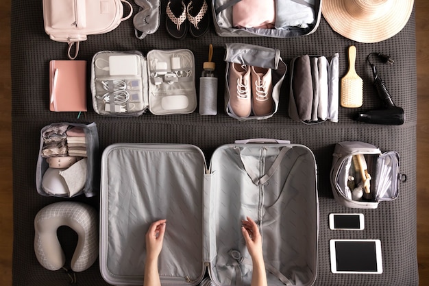 Vista de cima, mãos de mulher se preparando para a viagem de férias fazendo a mala usando o método konmari