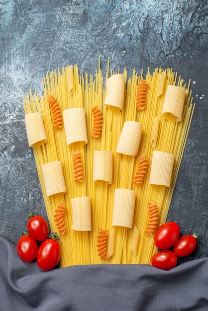 vista de cima massas crus espaguete rigatoni espirais tomate cereja xale roxo em fundo cinza