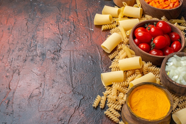 Vista de cima massas crus penne rigatoni espirais vegetais picados em tigelas na mesa de madeira