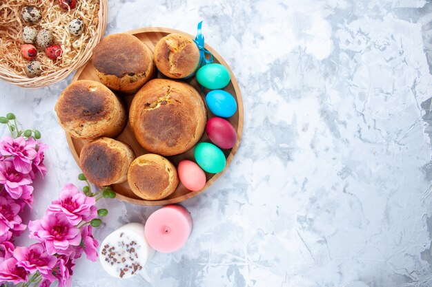 vista de cima ovos de páscoa coloridos com pão e bolos festivos dentro da bandeja na superfície branca