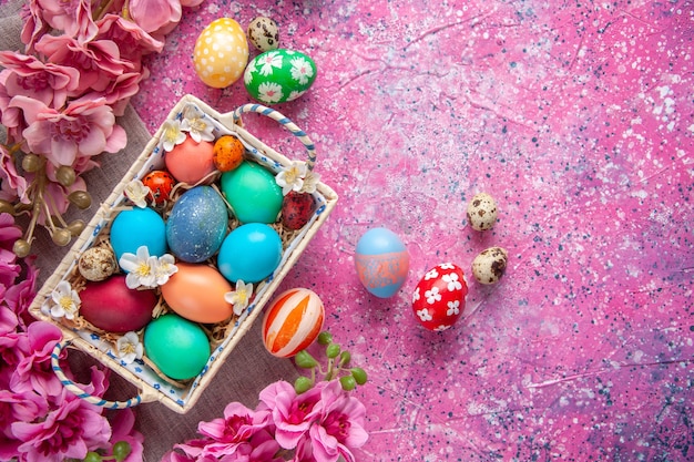 vista de cima ovos de páscoa coloridos dentro de uma caixa fofa com flores na superfície cor-de-rosa conceito de páscoa colorido ornamentado feriados primavera