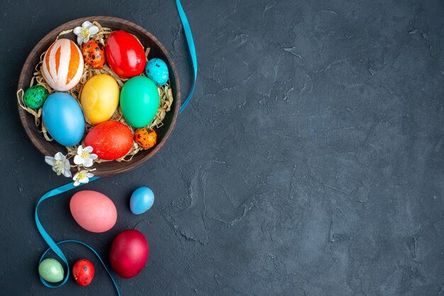 Vista de cima ovos de páscoa coloridos dentro do prato com canudo na superfície escura